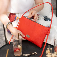 Load image into Gallery viewer, Person opening a red clutch bag with drinks on a table in the background