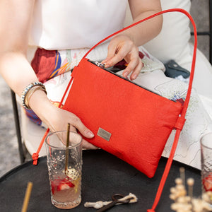 Person opening a red clutch bag with drinks on a table in the background